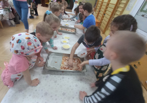 Dzieci posypują pizzę serem