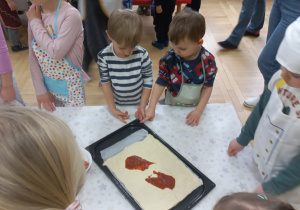 Dzieci wykładają sos na pizzę